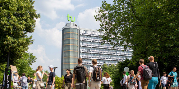 Foto: Der belebte Nordcampus der TU Dortmund an einem sonnigen Tag. Im Vordergrund sieht man Studierende und im Hintergrund sieht man den Mathetower.