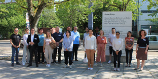 A group of people stands on the sunny campus of TU Dortmund University.