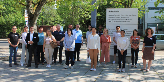 Eine Gruppe von Personen steht auf dem sonnigen Campus der TU Dortmund.