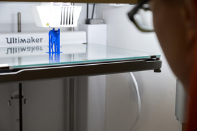 Der Druckkopf eines 3D-Druckers erzeugt eine blaue Figur auf eine Plattform.