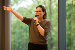 In the photo, you can see a woman with short dark hair speaking into a microphone.