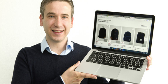 Dr. Sören Köcher holds up a laptop.