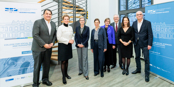 Eröffnung des College for Social Sciences and Humanities Gruppe von acht Personen im Foyer eines Gebäudes: RUB-Rektor Prof. Martin Paul, Ministerin Ina Brandes, Direktorin Prof. Julika Griem, UDE-Rektorin Prof. Barbara Albert, Prof. Ute Schneider, Prof. Friedrich Balke und Prof. Maximiliane Wilkesmann aus dem Scientific Board sowie TU-Rektor Prof. Manfred Bayer.