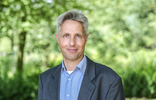 Frank Jenau Porträtbild von Frank Jenau mit grünen Bäumen im Hintergrund.