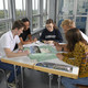 Auf dem Foto sieht man fünf Studierende, die am Tisch sitzen und gemeinsam ein Projekt bearbeiten.
