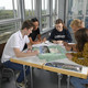 The photo shows five students sitting at a table working on a project together.