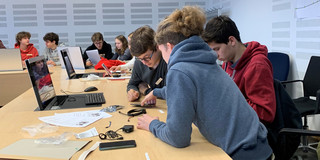 Jugendliche sitzen an einem Tisch und beschäftigen sich mit Elektroteilen.