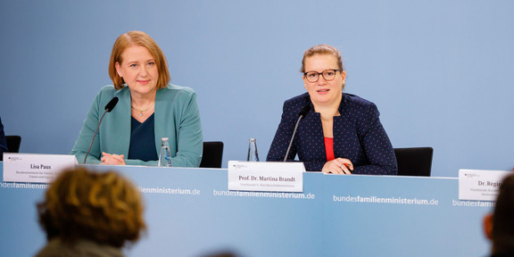 Foto: Drei Personen sitzen bei einer Pressekonferenz an einem Tisch und beantworten Fragen.