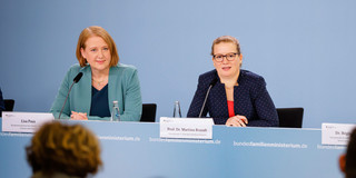 Foto: Drei Personen sitzen bei einer Pressekonferenz an einem Tisch und beantworten Fragen.