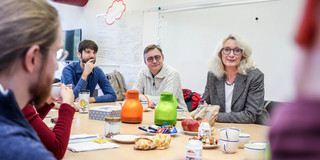Digital Lunch Mehrere Personen sitzen an einen reichlich gedeckten Tisch und unterhalten sich.