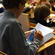 Einführung Teilnehmerin schaut die Inhalte der Teilnehmer*innen-Mappe im Hörsaal an. Weitere Teilnehmende im Hintergrund.