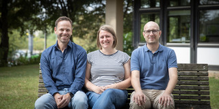 Three people are sitting on a bench in front of the EF50 building.