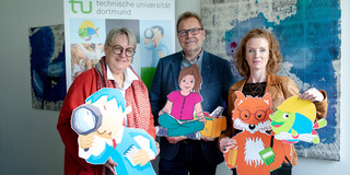 Prof. Prof. Barbara Welzel, Prof. Thomas Goll and Svenja Sayk stand in front of a large KinderUni display.