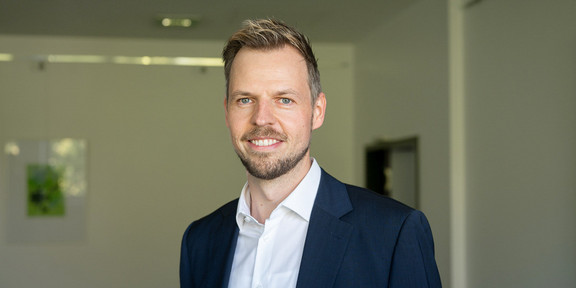 Zu sehen ist ein Porträtfoto von Prof. Peitz in einem Raum mit weißen Wänden im Hintergrund.