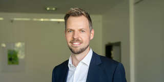 Zu sehen ist ein Porträtfoto von Prof. Peitz in einem Raum mit weißen Wänden im Hintergrund.