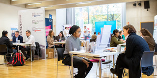 In a large room there are many tables where people are having conversations