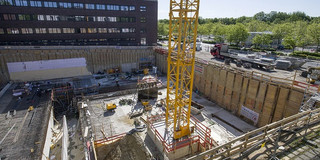 Eine Baustelle in einem Fundament eines neuen Gebäudes, darin befinden sich ein großer Kran, Bauarbeiter und Baumaterial.