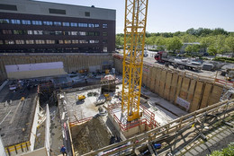Eine Baustelle in einem Fundament eines neuen Gebäudes, darin befinden sich ein großer Kran, Bauarbeiter und Baumaterial.