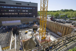 Eine Baustelle in einem Fundament eines neuen Gebäudes, darin befinden sich ein großer Kran, Bauarbeiter und Baumaterial.