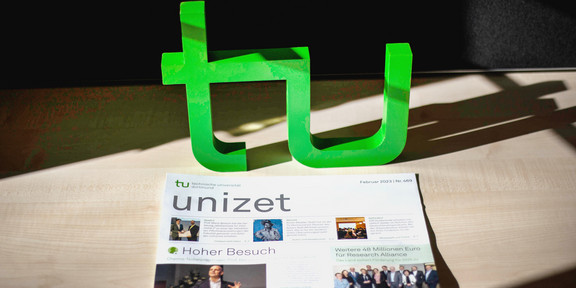 The February 2023 issue of unizet is on the floor. Behind it are the two letters t and u.
