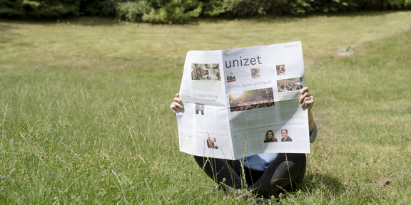 A person sits on a lawn and reads the new unizet issue