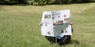 Eine Person sitzt auf einer Wiese und liest die neue unizet-Ausgabe