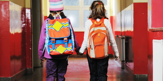 Das Foto zeigt zwei kleine Mädchen, die händchenhaltend durch den Flur in einer Schule gehen. 
