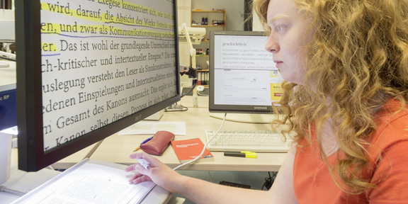 A woman with visual or reading disabilities sits in front of a computer screen.