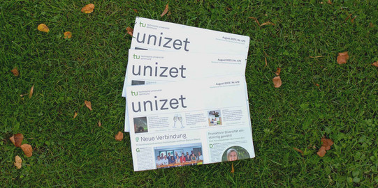 unizet_August_2023 Drei Ausgaben der unizet von August 2023 liegen gefächert übereinander im Gras.