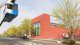 Juli Das rot verklinkerte Internationale Begegnungszentrum auf dem Campus Nord. Im Vordergrund fährt die H-Bahn.