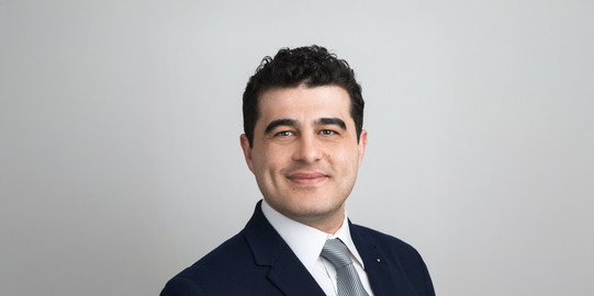 Porträtfoto von Prof. Onur Günlü: Prof. Günlü trägt einen Anzug und steht vor einem hellgrauen Hintergrund und lächelt in die Kamera.