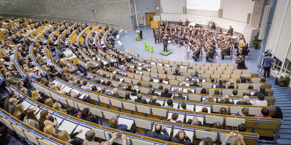 28-11-19-Akademische-Jahresfeier Das vollbesetze Audimax mit einer Bläsergruppe vorne.