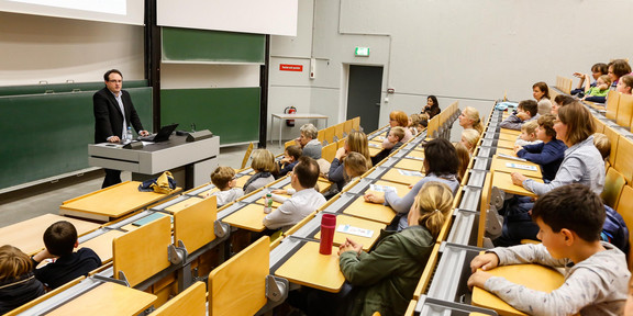 Kinder und Eltern verfolgen eine Vorlesung in einem Hörsaal