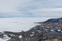 Zahlreiche kleinere Gebäude und Container auf brauner Erde vor einem Eisschelf.