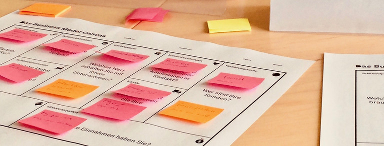 Auf einem Schreibtisch liegen diverse Zettel und Arbeitsmaterialien, die mit bunten Post-Its versehen sind und Notizen enthalten. 