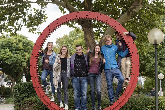 Fakultät Maschinenbau Studentinnen und Studenten stehen in einem großen Zahnrad