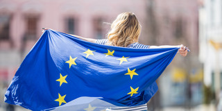 A woman is holding a European flag with her hands outstretched, waving it behind her back.