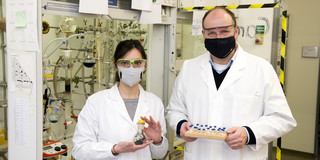 A woman and a man with lab coats and safety goggles standing in a chemistry lab.