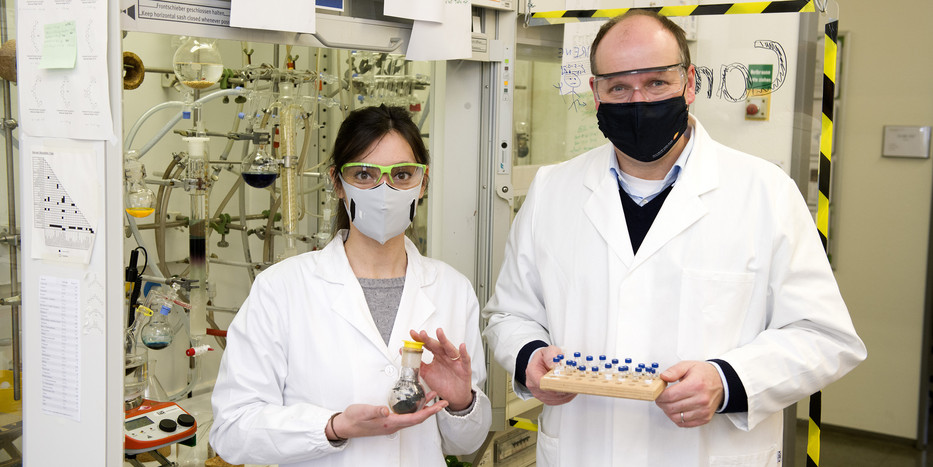 A woman and a man with lab coats and safety goggles standing in a chemistry lab.