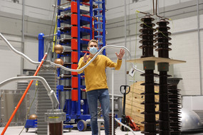 Ein Mann steht zwischen Aufbauten für ein elektrotechnisches Experiment.
