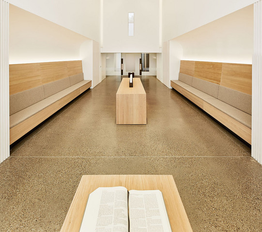 Auf dem Foto sieht man einen hellen, modernen Raum mit hohen Decken und Sitzbänken.