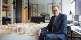Portrait von Christoph Mäckler neben einem architektonischen Modell von Gebäuden. 