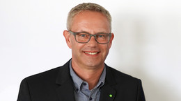 September Foto: Ein Mann mit Brille lächelt vor weißem Hintergrund in die Kamera.