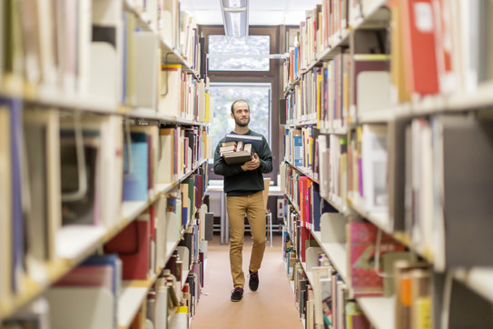 Student in der Universitätsbibliothek mit Büchern im Arm