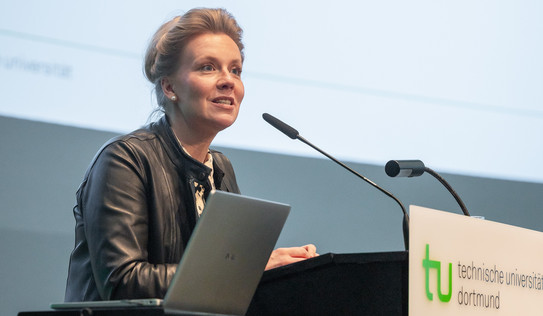 Photo: A person speaks at the podium of TU Dortmund University, with a laptop and microphone in front of them.