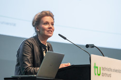 Foto: Eine Person spricht am Pult der Technischen Universität Dortmund, vor ihr ein Laptop und Mikrofon.