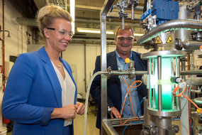 Prof. Gerhard Schembecker und Ina Brandes stehen mit Schutzbrille vor einer Apparatur in einem Labor.. 