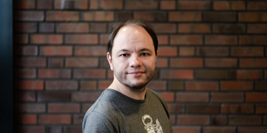 Prof. Marc Aßmann Ein Porträtbild von einem Mann, Prof. Marc Aßmann vor einer Wand aus Klinkern.