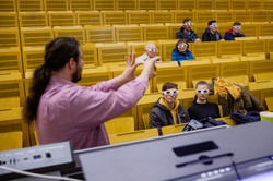 Menschen mit Schutzbrillen in einem Hörsaal. Im Vordergrund ein Mann, der etwas erklärt.