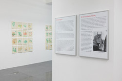 Ausstellung Goldenes Wunder Zwei Info- und Hinweistafeln hängen an einer rechten Wand. An der linken Wand befinden sich Bilder/Kunstwerke.